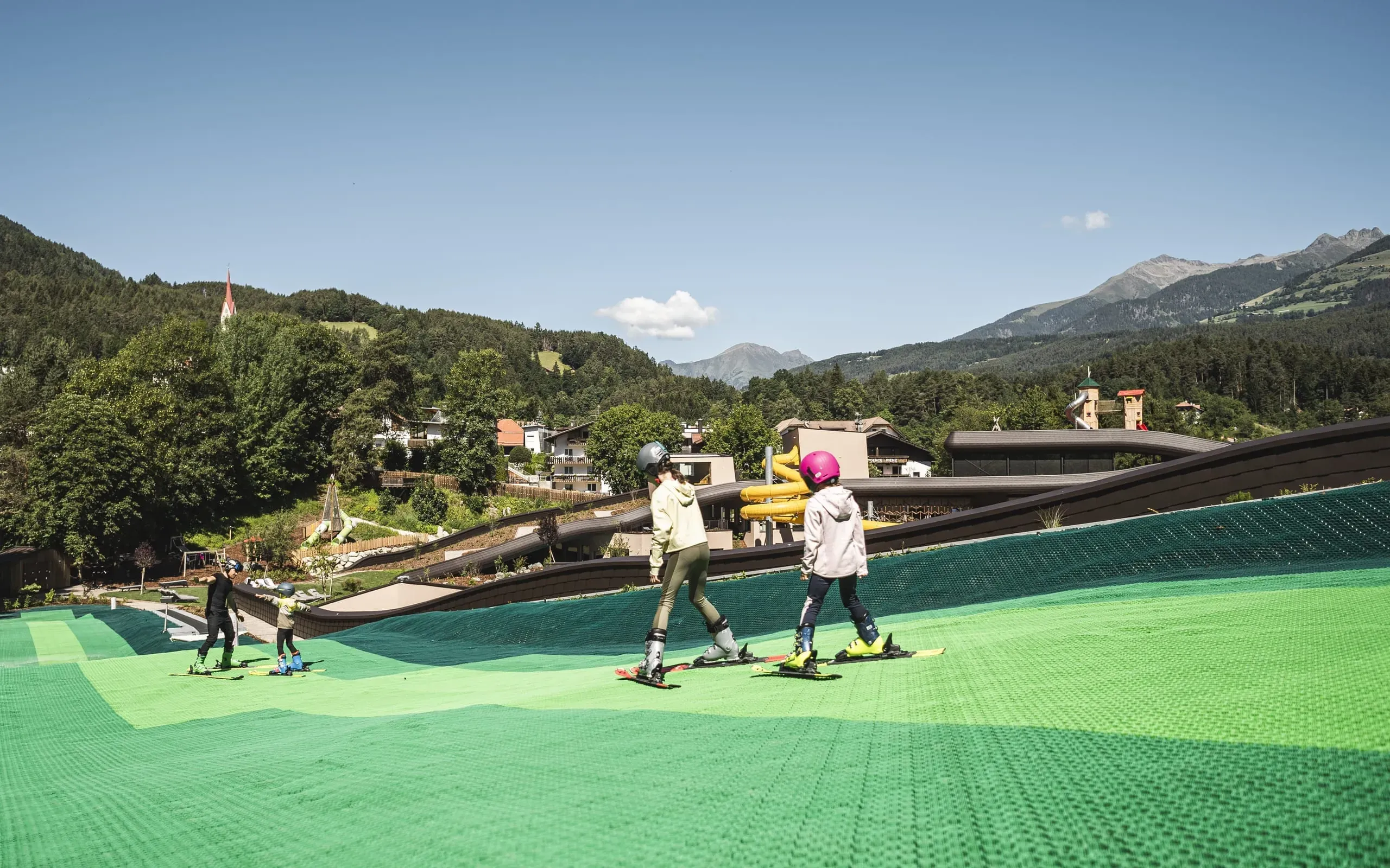 Kinder sausen die Skipiste auf dem Dach des Falkensteiner Family Resort Lido herunter.