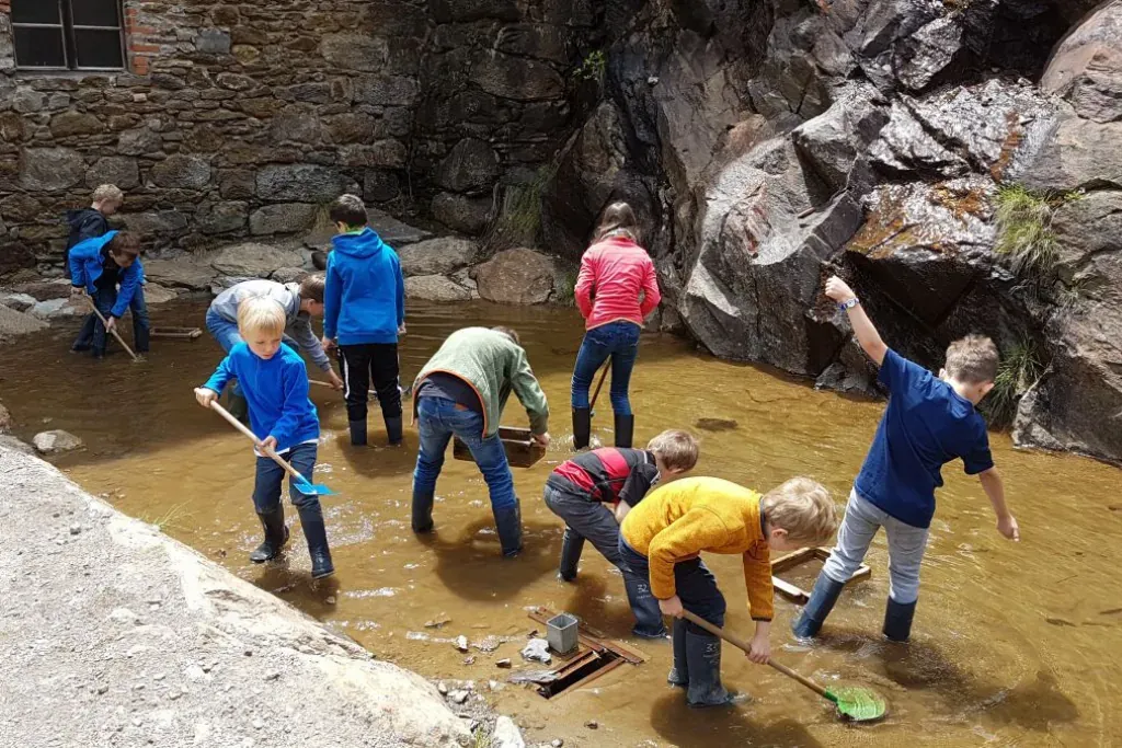 Kinder suchen im Rahmen der Betreuung im Hotel Alpin nach verborgenen Schätzen in einem Bach.