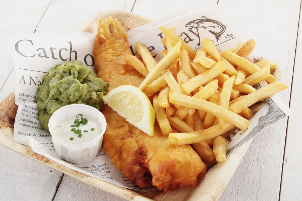 Klassische Fish and Chips, knuspriger frittierter Fisch und goldene Pommes Frites, serviert mit Zitrone und Remoulade, als typisches Gericht der englischen Küche.