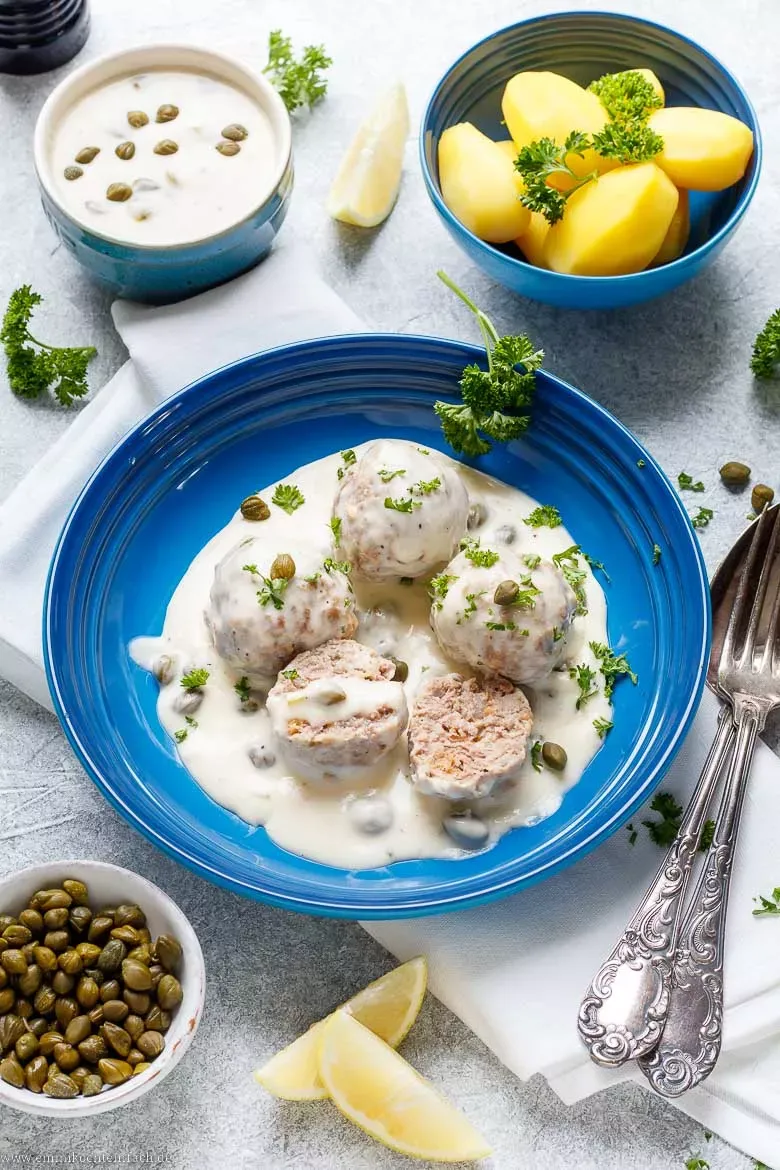 Klassische Königsberger Klopse mit cremiger Kapernsoße und Petersilie auf einem Teller, serviert mit Salzkartoffeln.