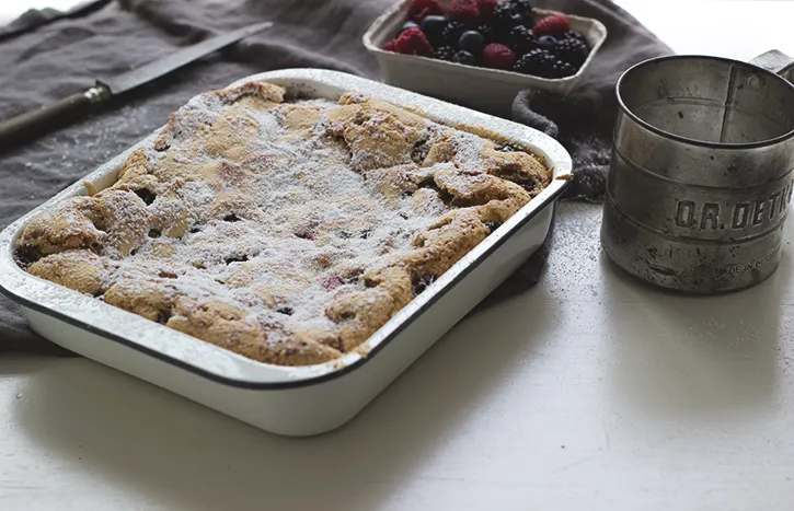 Klassischer deutscher Beerenkuchen vom Blech, bestreut mit Puderzucker und verschiedenen Waldbeeren, ideal zur Kaffeetafel.