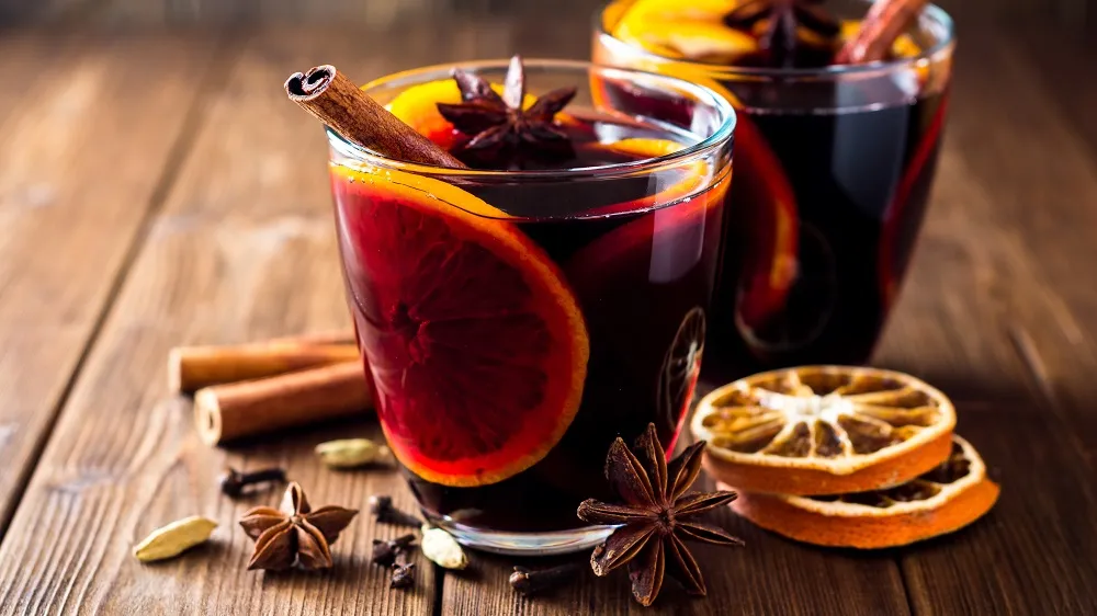 Klassischer roter Glühwein in zwei Gläsern, verziert mit Orangenscheiben, Zimtstangen und Sternanis auf einem Holztisch
