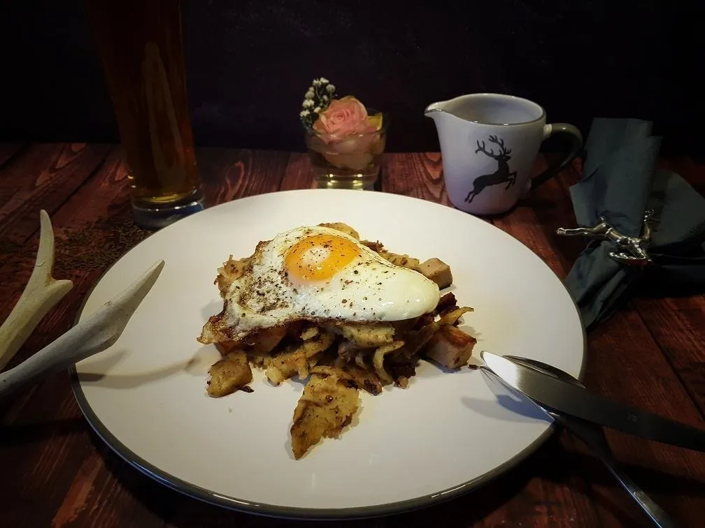 Klassisches Tiroler Gröstl mit Spiegelei und krossen Semmelknödeln auf einem Teller angerichtet