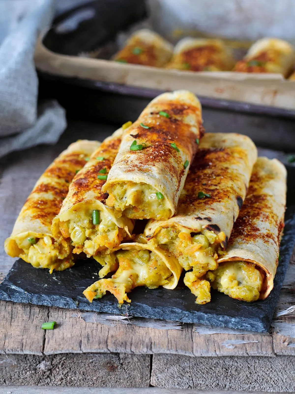 Knusprige vegane Gemüse-Taquitos mit Kartoffel-Gemüsefüllung auf einem schwarzen Brett, ideal für unterwegs oder zu Hause.