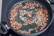Knuspriger Speck und aromatischer Knoblauch werden in der Pfanne angebraten, um dem Carbonara Rezept Tiefe zu verleihen.