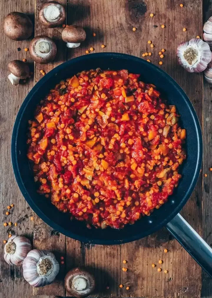 Kochprozess der veganen Linsen Bolognese Soße mit Zwiebeln, Karotten und Linsen in einem Topf