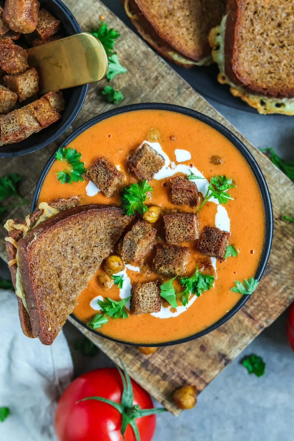 Köstliche vegane Tomatensuppe, ideal für kalte Tage, garniert mit frischen Kräutern und einem bunten Mix aus knusprigen Beilagen.