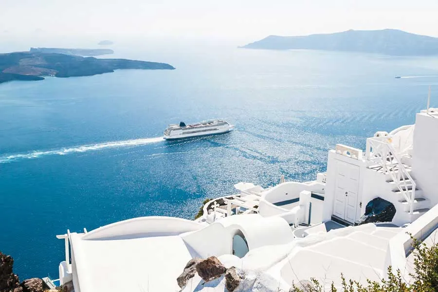 Kreuzfahrtschiff vor der malerischen Küste Santorins mit weißen Häusern