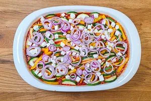 Kritharaki-Auflauf mit Zwiebelringen und Feta toppen