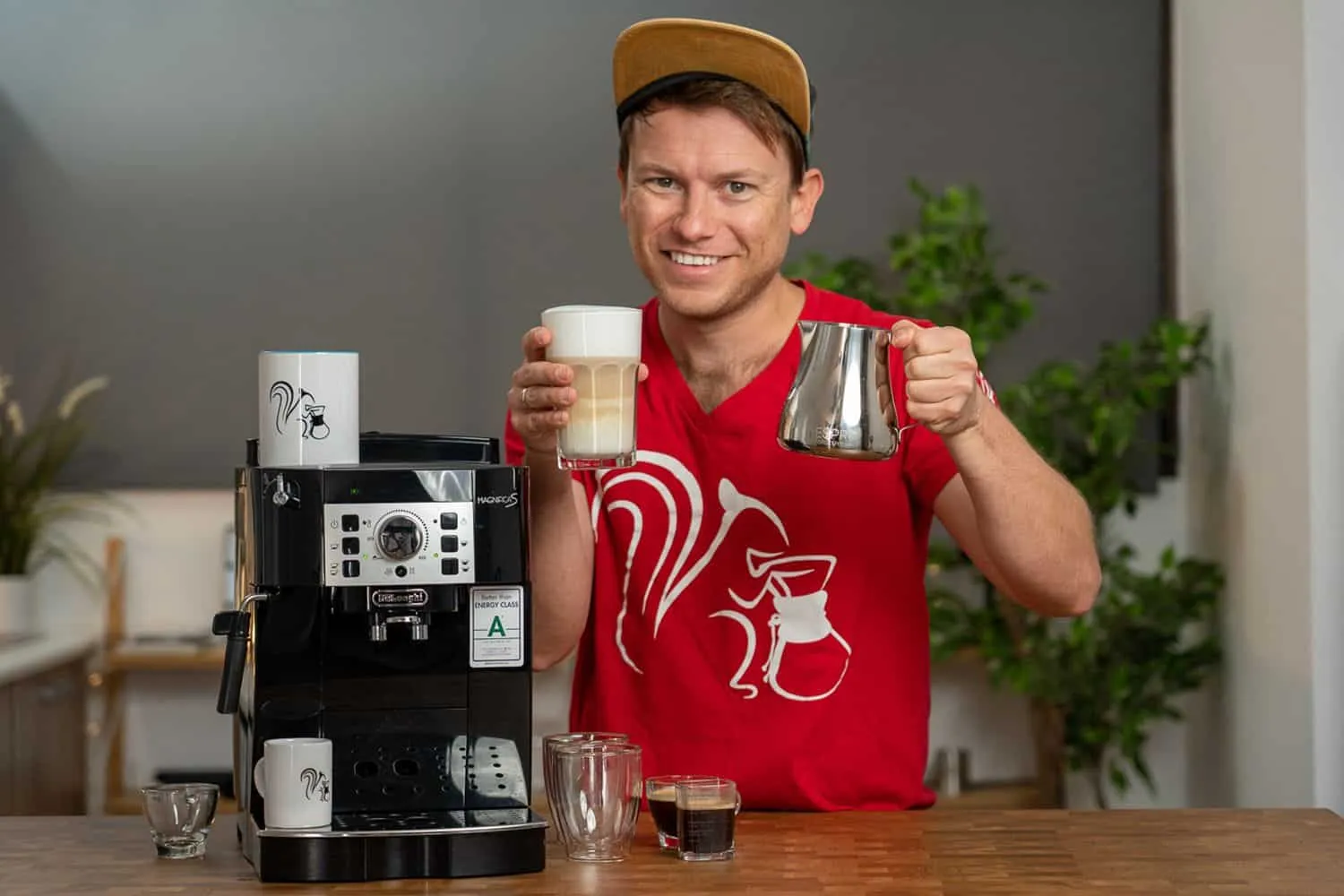 Lachender Mann mit DeLonghi ECAM 22.110.B, daneben ein fertiger Latte Macchiato