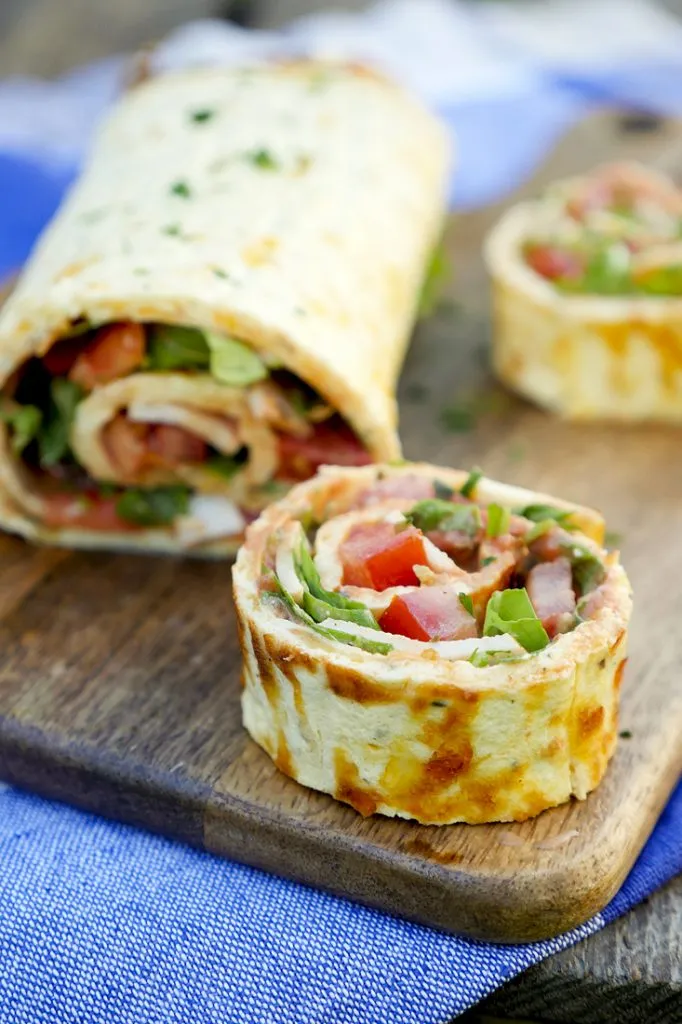 Low Carb Pizzarolle mit Rucola, Tomaten und Pute auf einem Holzbrett