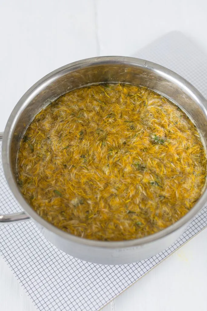 Löwenzahnblüten und Zitronen im Kochtopf während des Ziehens für den Sirup