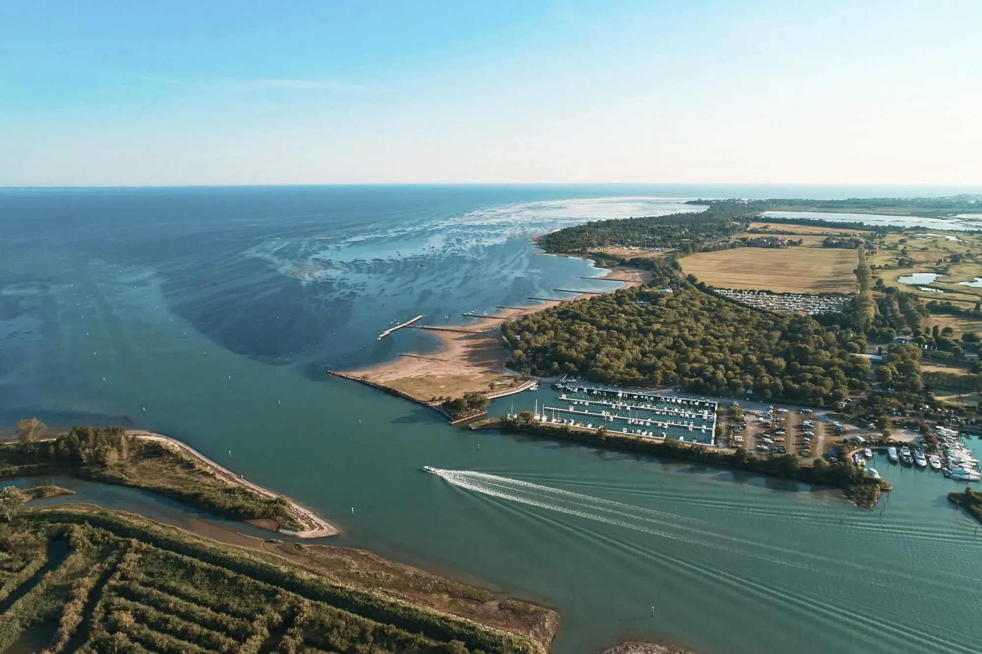 Luftaufnahme der Küstenlandschaft mit Blick auf das weite Meer und den Yachthafen, in unmittelbarer Nähe des Club del Sole Tenuta Primero Grado Family Collection, ideal für Wasseraktivitäten mit oder ohne Hund.
