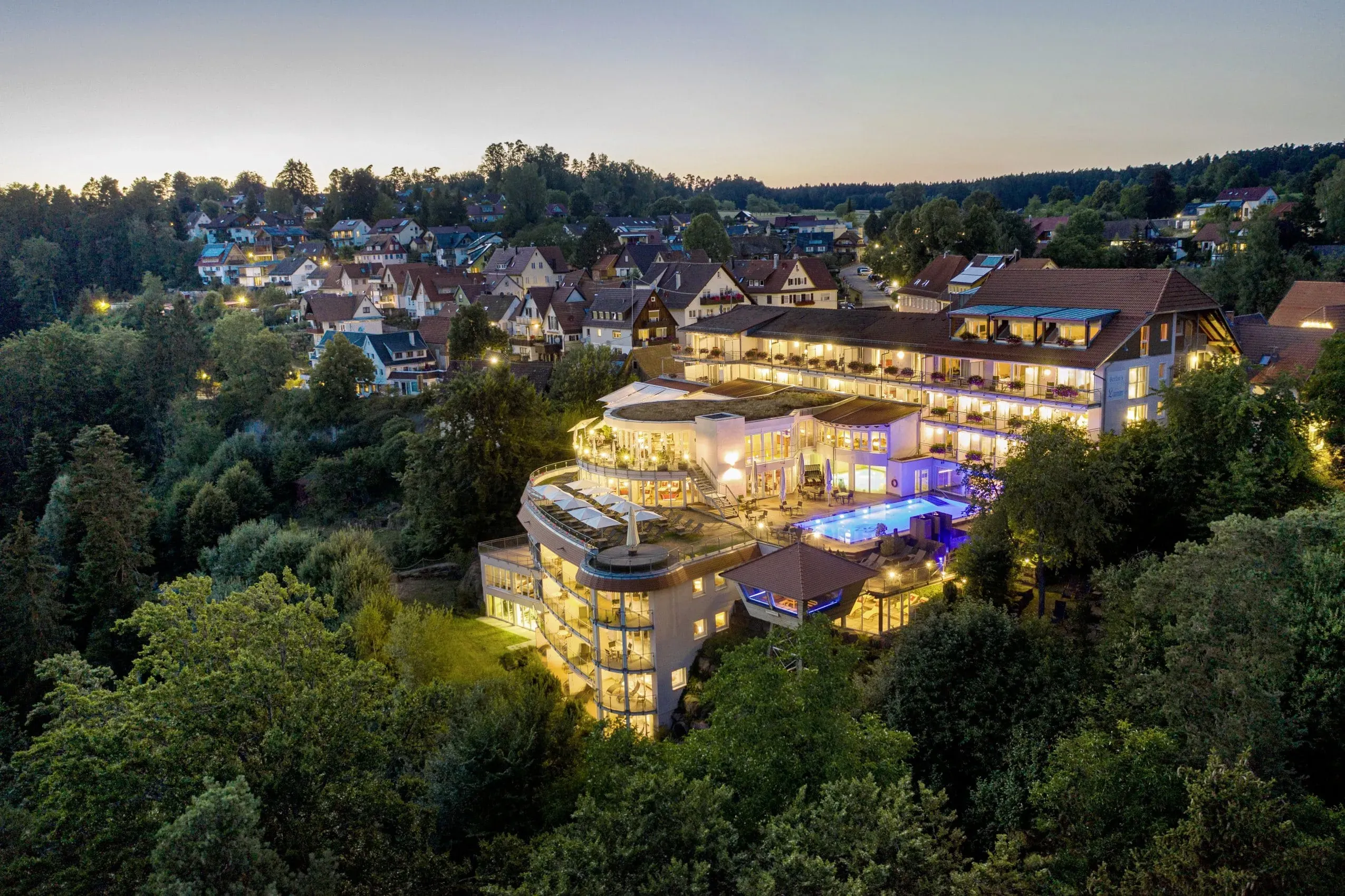 Luftaufnahme des beleuchteten Wellnesshotels Kronelamm in Bad Teinach-Zavelstein bei Dämmerung, umgeben von der beeindruckenden Schwarzwald-Landschaft, ideal für einen Urlaub mit Hund.