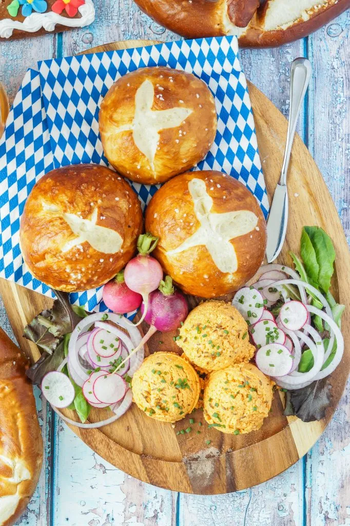 Luftaufnahme von drei Kugeln Obazda (bayerischer Käse- und Bier-Dip) auf einem Holzbrett mit blau-weißen Servietten.
