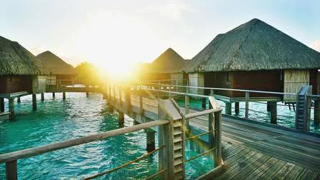 Luxuriöse Overwater-Bungalows auf Bora Bora in Französisch-Polynesien bei Sonnenuntergang, mit einem ruhigen türkisfarbenen Meer.