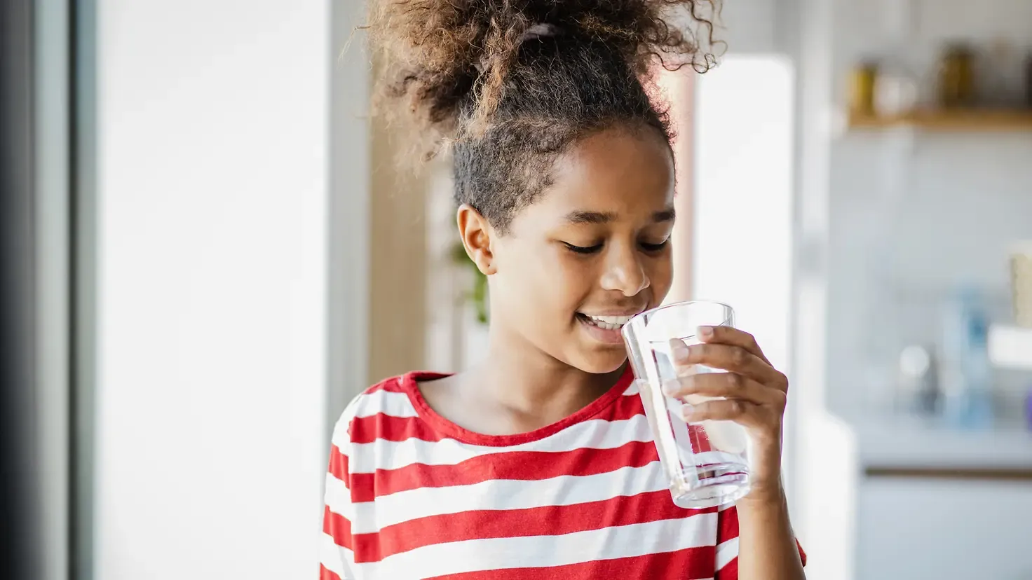 Mädchen trinkt ein Glas reines Wasser – der ideale, gesunde Durstlöscher für Kinder und Erwachsene.