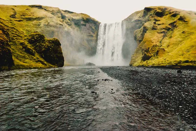 Malerische Landschaft Islands im Juli mit grünen Hügeln, einem Fluss und schneebedeckten Bergen im Hintergrund – ein idealer Reisetipp für Naturliebhaber.