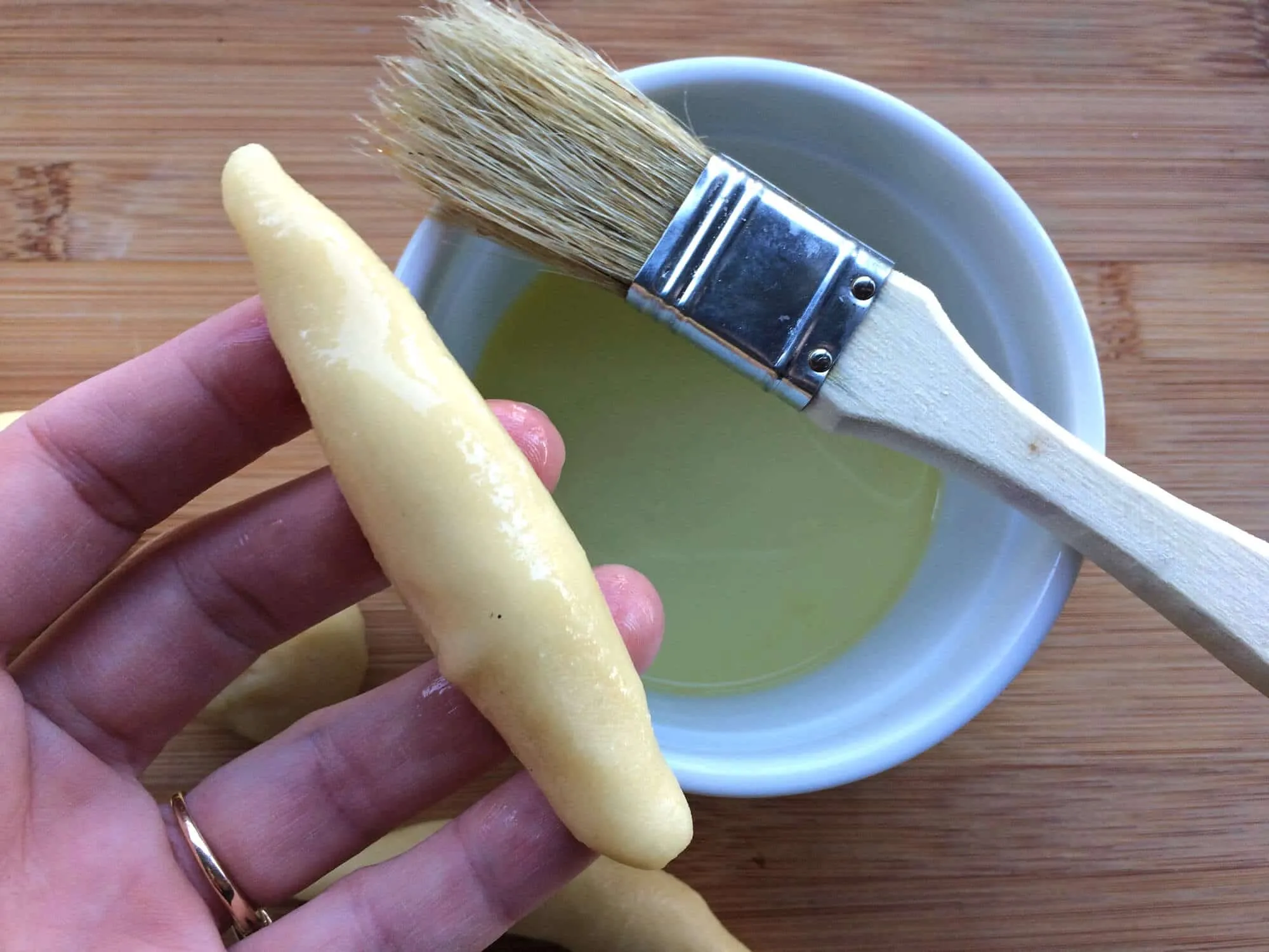 Mandelhörnchen-Rohlinge werden mit Eiweiß bestrichen, bevor sie in Mandelsplittern gerollt werden