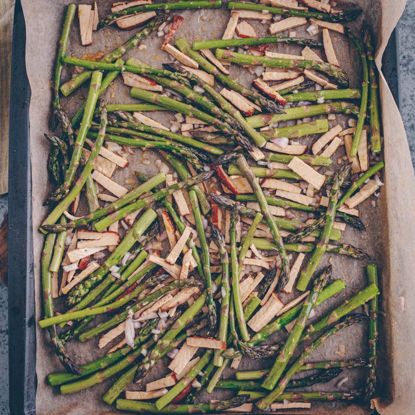 Marinierter grüner Spargel und Taifun Räuchertofu mit Zitrone und Gewürzen auf einem Backblech