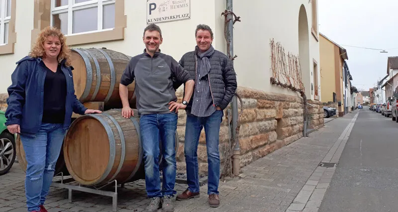 Mathias Finck, Gründer von Spar mit! Reisen, im Gespräch mit Winzer Frank Hemmes und Ellen Pohl vor einem Weinfass am Rhein, symbolisch für die persönliche Qualitätsprüfung von spar mit com.