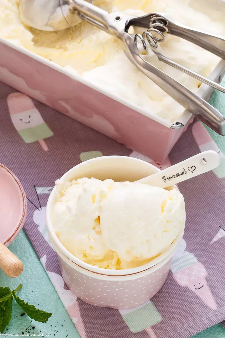 Mehrere Kugeln cremig-glattes Vanilleeis mit Kondensmilch, serviert mit einem Eislöffel