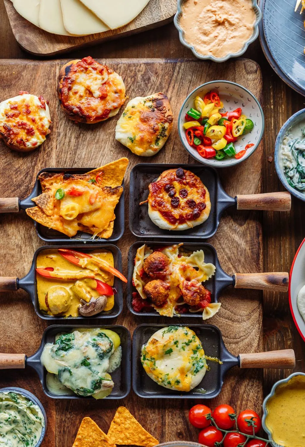 Mehrere Raclette-Pfännchen mit geschmolzenem Käse und blubbernden Zutaten