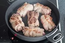 Mehrere Rinderrouladen werden in einem Bräter scharf angebraten, um eine goldbraune Kruste zu entwickeln.