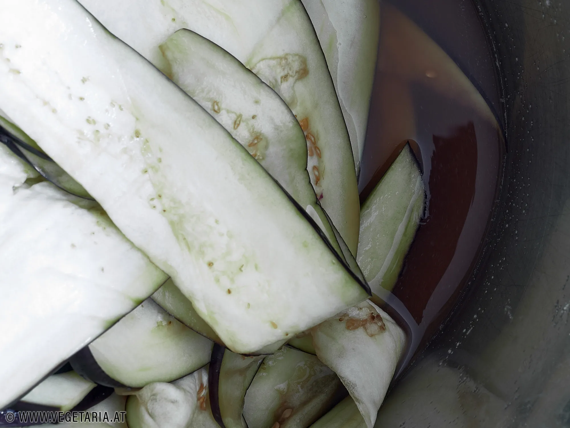 Melanzanischeiben, dünn geschnitten und gesalzen, liegen auf einem Schneidebrett. Das Salz beginnt, Feuchtigkeit zu ziehen.