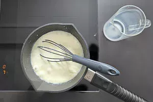 Milch wird langsam in die Mehlschwitze gegossen und mit einem Schneebesen für die Béchamelsauce verrührt