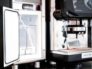 Milchschlauch eines Kaffeevollautomaten taucht in einen Milchbehälter ein, um frische Milch anzusaugen