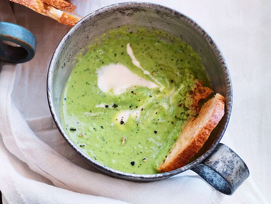 Minzige Erbsensuppe in einer stilvollen Schale, garniert mit frischer Minze und einem Klecks Crème fraîche, daneben geröstetes Brot.