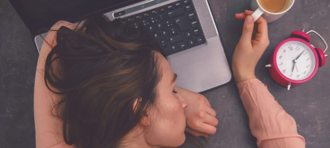 Müde Frau liegt auf Laptop, sucht nach Vitaminen gegen Müdigkeit