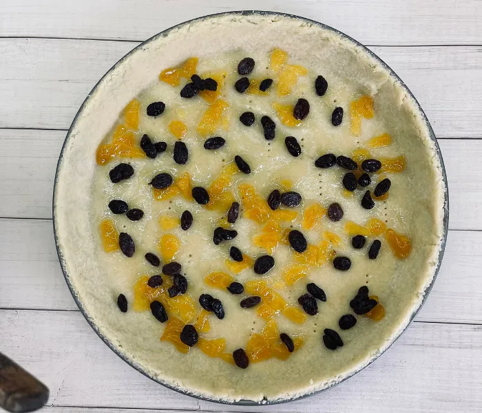 Mürbeteigboden eines Osterkuchens, bestrichen mit Aprikosenmarmelade und Rosinen