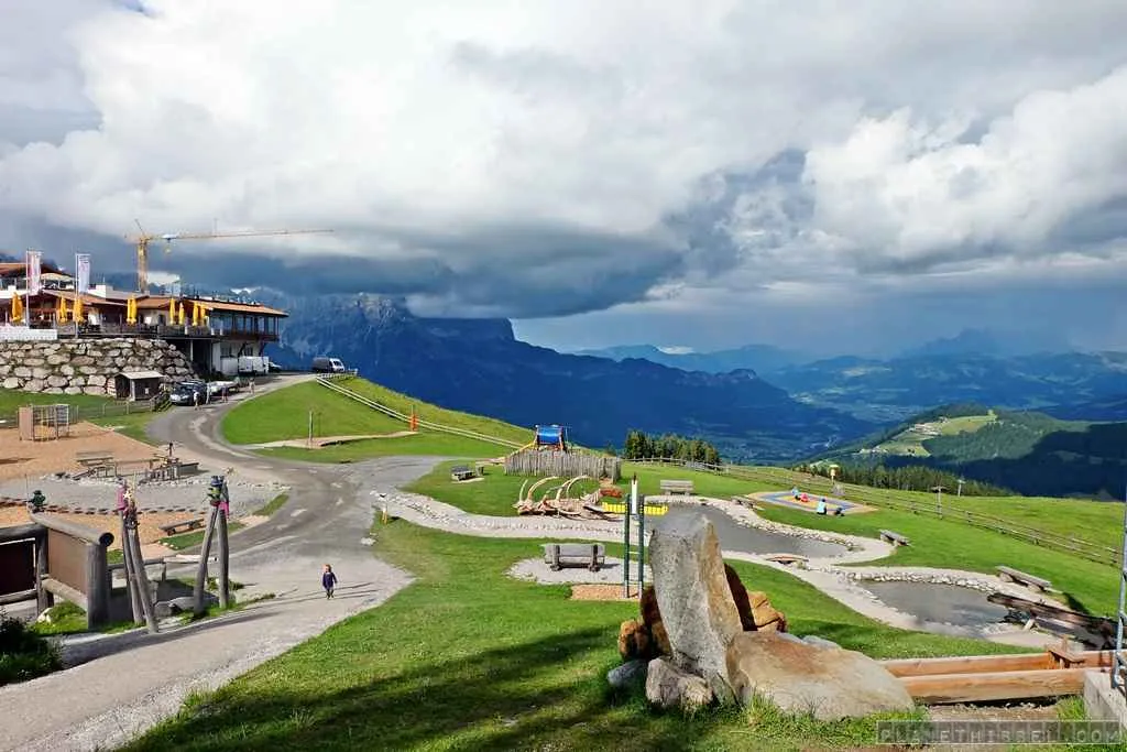 Mutter entspannt auf einem Liegestuhl mit Blick auf die Berge, während ihr Kind im Hintergrund spielt