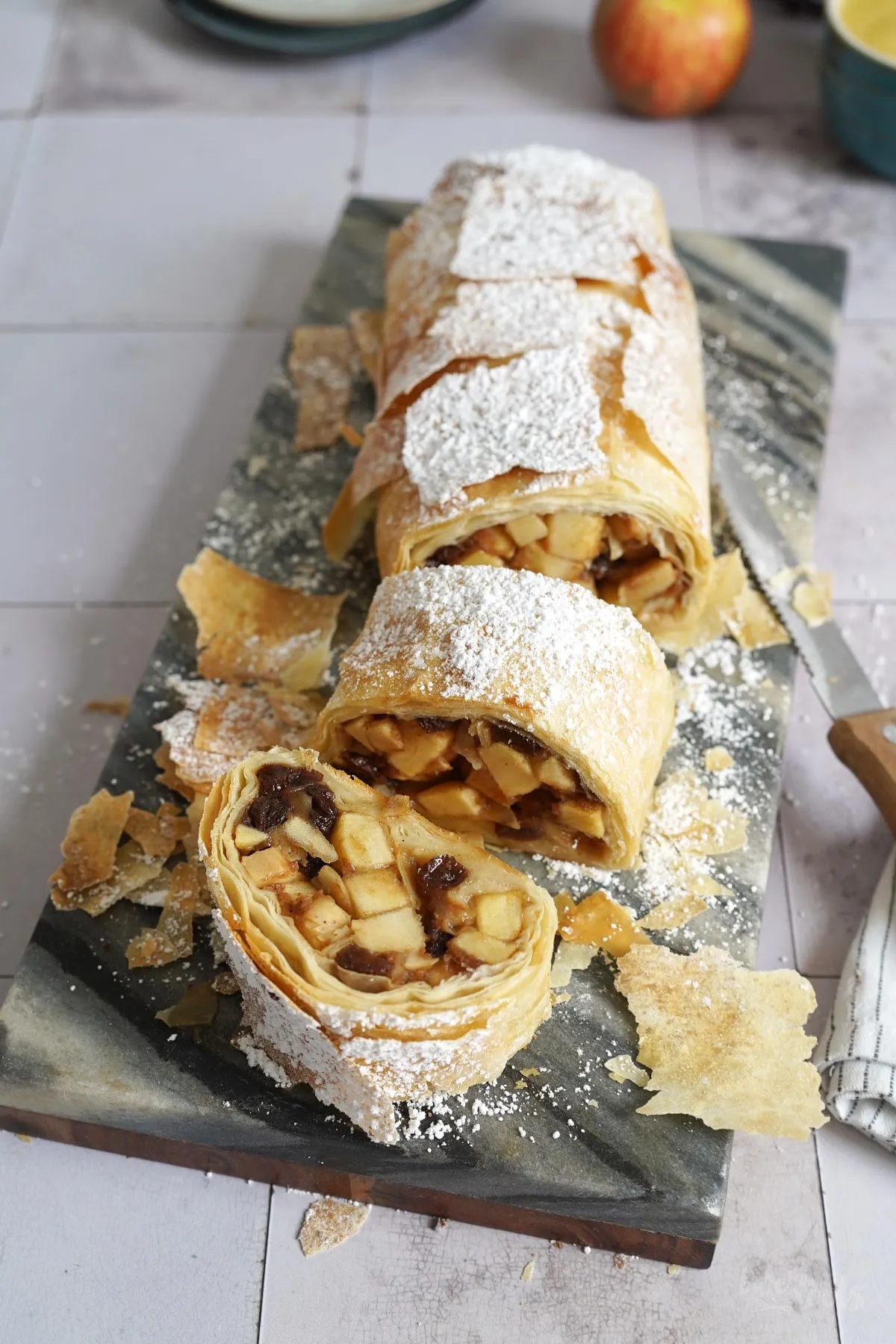 Nahaufnahme der Apfelfüllung mit Rum-Rosinen und Mandeln, umhüllt von mehreren dünnen Schichten Filoteig, bereit zum Rollen.