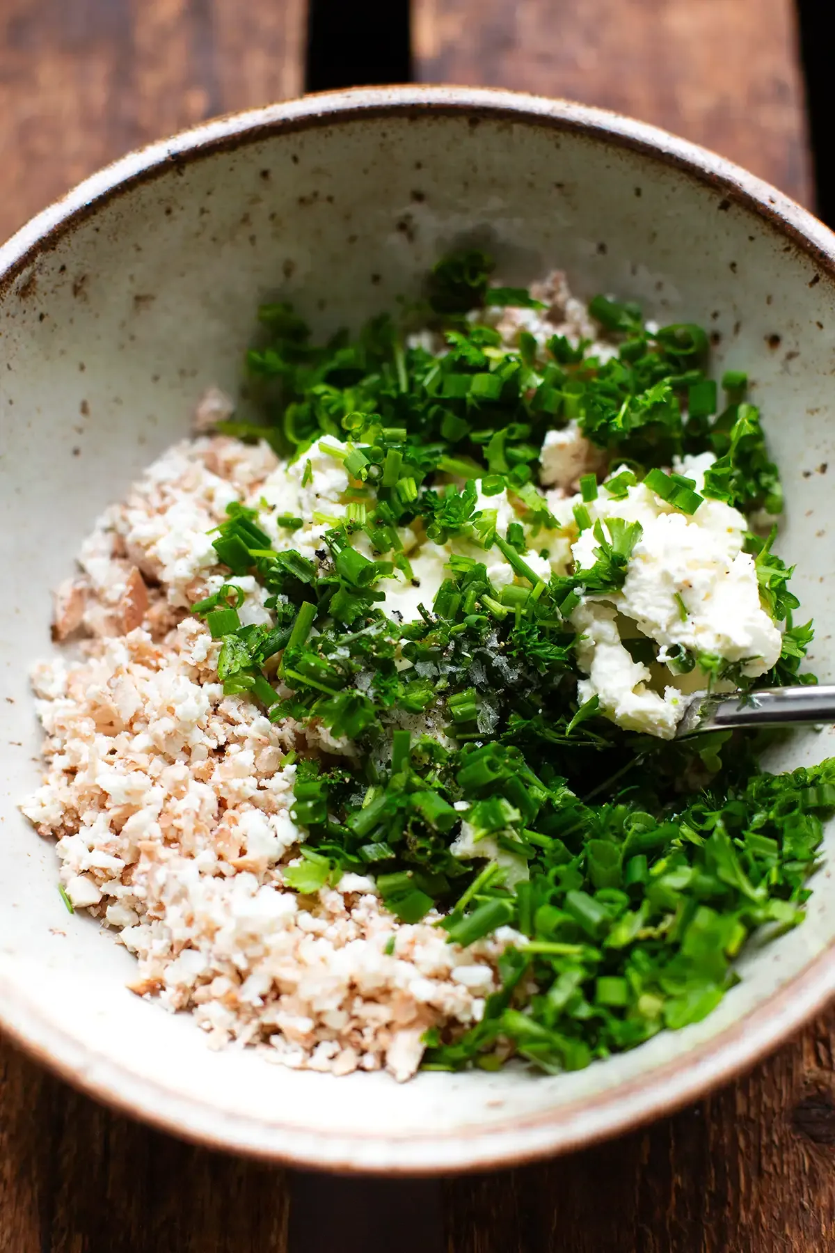 Nahaufnahme der cremigen Füllung für die Champignons, bestehend aus gehackten Pilzstielen, zerbröseltem Feta, Frischkäse und frischen Kräutern.
