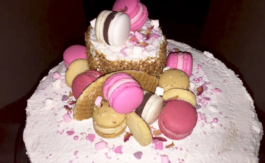 Nahaufnahme der exquisiten Tortendekoration mit rosa Luxemburgerli, Zuckerblüten und einem kleinen Küchlein als &quot;zweiter Stock&quot; auf dem Geburtstagskuchen.