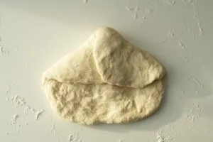 Nahaufnahme des Baguette-Teigs beim ersten Falten der linken Ecke, um eine optimale Struktur zu entwickeln.