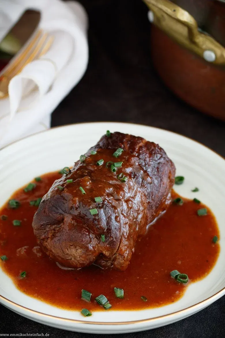 Nahaufnahme einer aufgeschnittenen Rinderroulade, die herzhafte Füllung ist sichtbar, umgeben von dunkler Bratensoße.