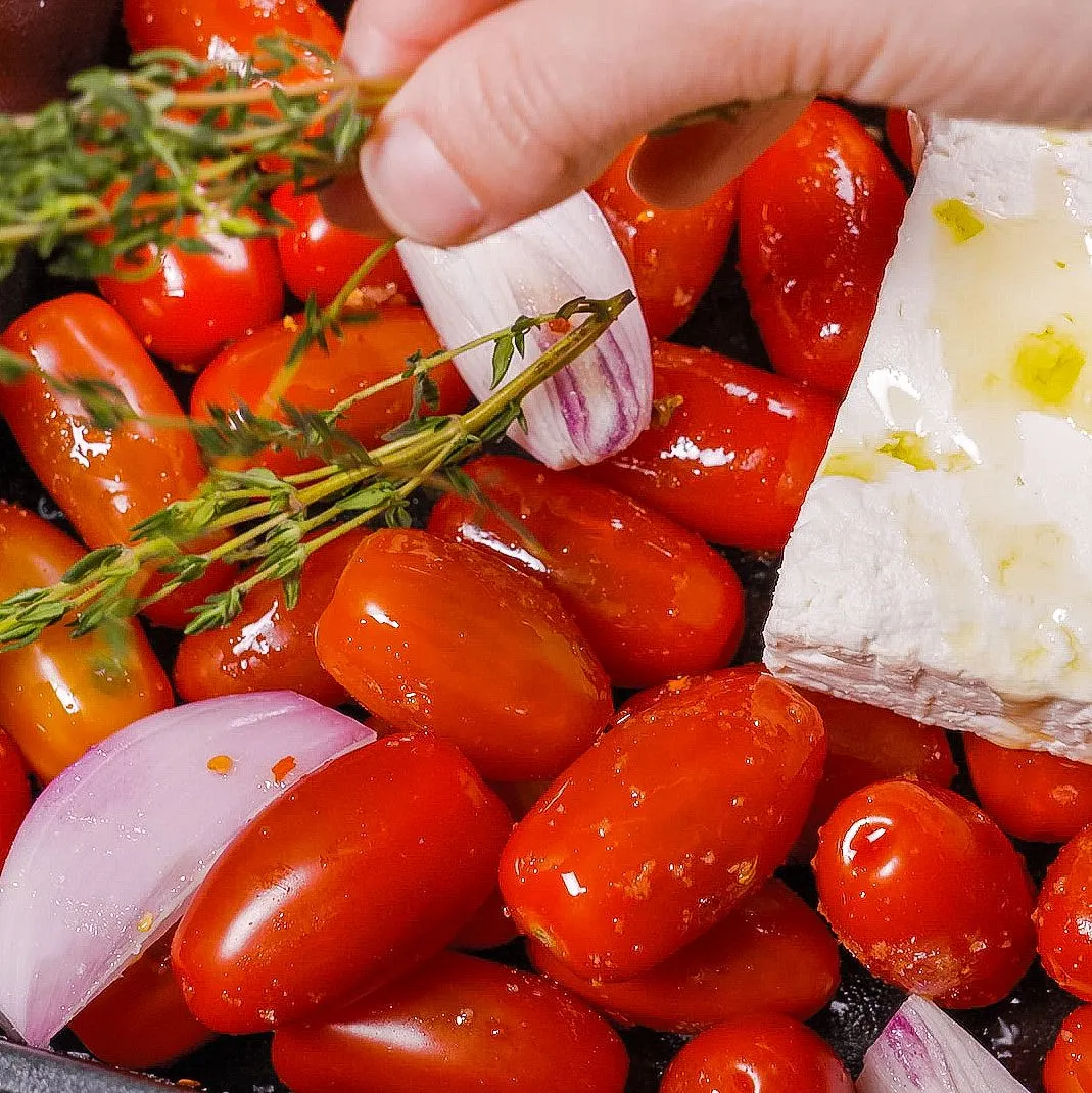 Nahaufnahme einer Auflaufform mit Schafskäse, Kirschtomaten und frischen Thymianzweigen, vor dem Backen für ein One Pot Nudelgericht.