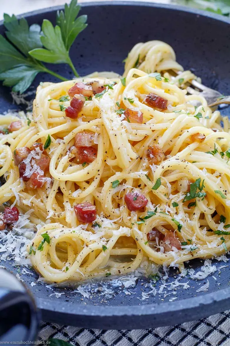 Nahaufnahme einer cremigen Original Carbonara ohne Sahne, mit knusprigem Speck und frischen Kräutern, bereit zum Genießen.