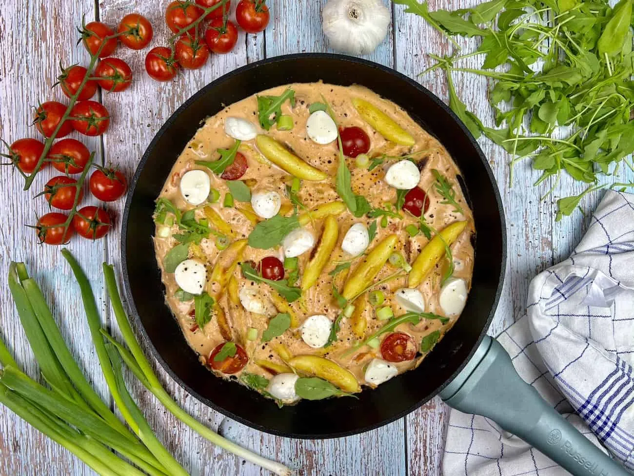 Nahaufnahme einer cremigen vegetarischen Schupfnudel-Pfanne mit Tomaten, Mozzarella und Rucola.