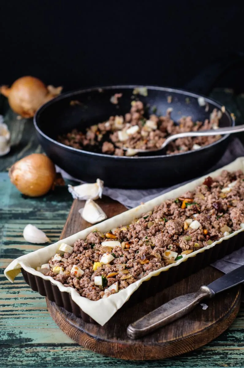 Nahaufnahme einer Empanada mit Blätterteig-Muster, angerichtet auf einem Holztisch für festliche Anlässe