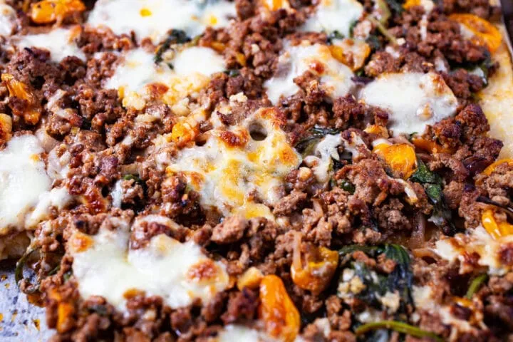 Nahaufnahme einer fertig gebackenen Polenta Pizza mit geschmolzenem Käse, Hackfleisch und knackigem Gemüse.