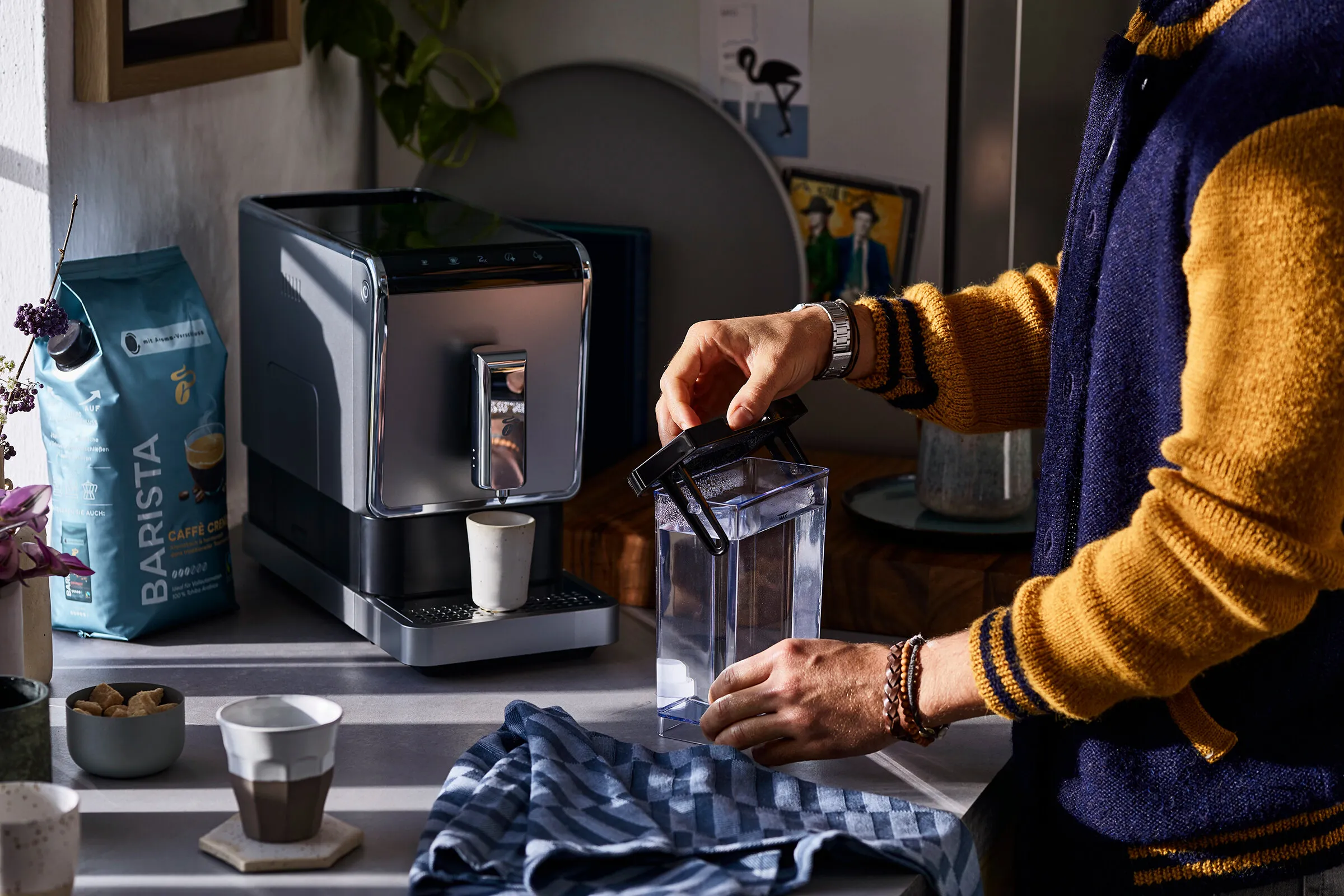 Nahaufnahme einer Hand, die das Display einer silbernen Tchibo Kaffeevollautomat Maschine bedient, um den Entkalkungsvorgang zu starten oder zu überprüfen.