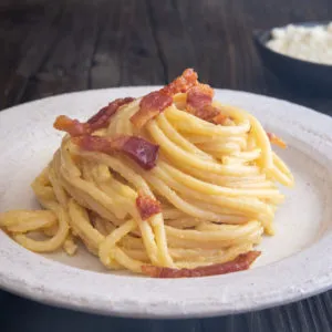 Nahaufnahme einer Portion Carbonara auf einem Teller, garniert mit Guanciale und schwarzem Pfeffer