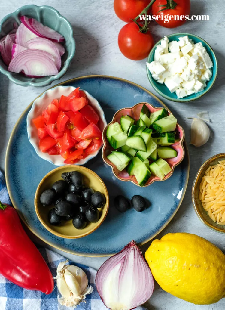 Nahaufnahme einer Portion griechischen Nudelsalats mit Kritharaki, Feta und frischem Gemüse, garniert.