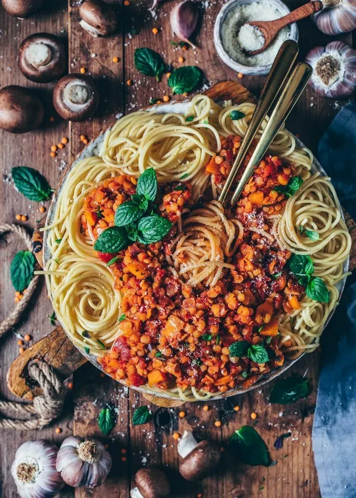 Nahaufnahme einer Portion Linsen Bolognese auf Spaghetti, garniert mit frischer Petersilie und veganem Parmesan
