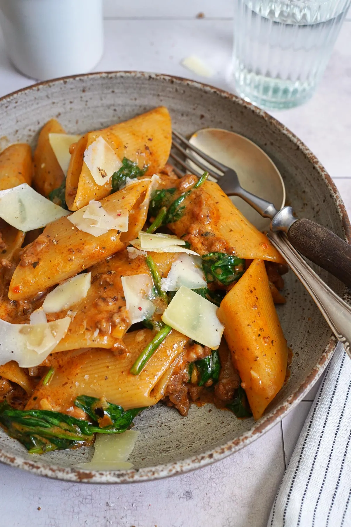 Nahaufnahme einer Portion One-Pot Pasta mit Spinat, Hackfleisch und Tomatenpesto, garniert mit Parmesan auf einem Teller.